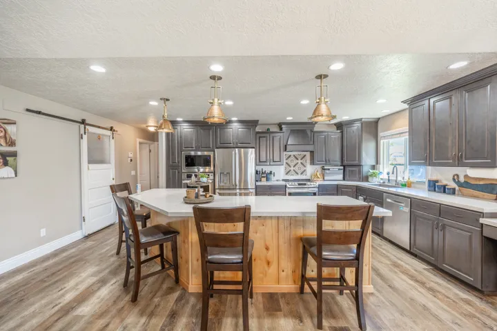 Spacious kitchen featuring an extended island with a light wood finish, recessed lighting, actual reclaimed marine pendant lights, dark wood-finish cabinetry, and stainless steel appliances