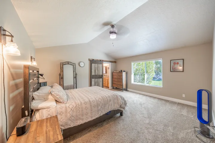 Primary suite with vaulted ceilings, carpeted flooring, and a ceiling fan with integrated lighting