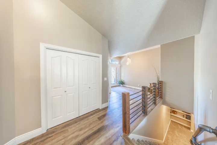 Vaulted ceiling, wood-finish flooring, white bi-fold doors, wood and metal railing, and built-in shelving