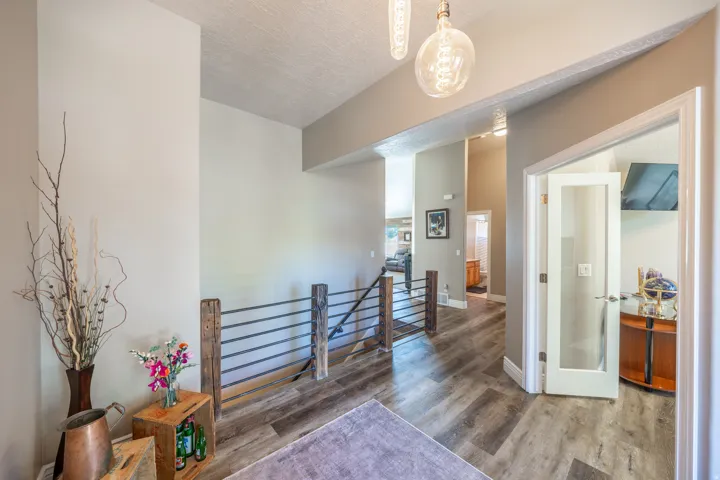 Wood-finish flooring, industrial-style railing with wood newel posts, contemporary pendant lighting, and a glass-paneled door