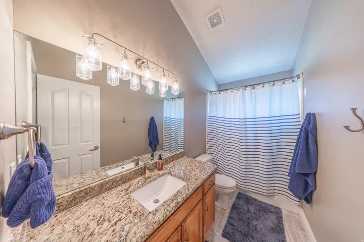 Vaulted ceiling bathroom featuring a vanity with a stone countertop, an undermount sink, and wood cabinetry
