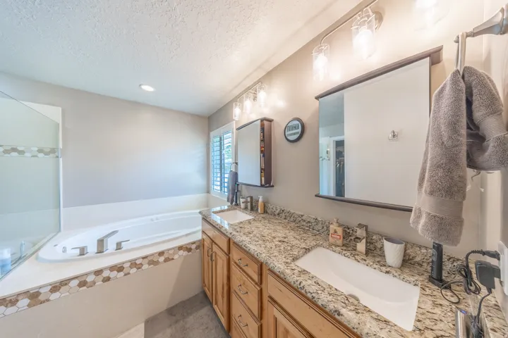 Primary suite bathroom with Dual vanity with granite-finish countertops, undermount sinks, and wood cabinetry, separate jetted tub and shower and a heated towel rod.