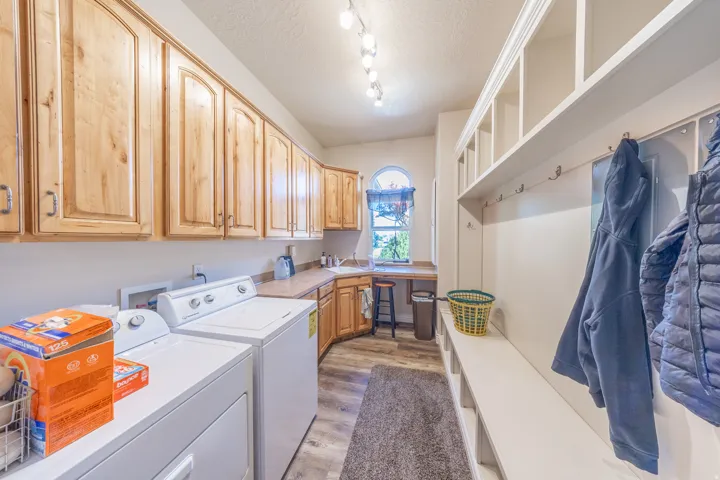 Laundry and mudroom combination with wood-finish flooring, extensive built-in cabinetry, a utility sink, and a built-in bench with storage cubbies and coat hooks