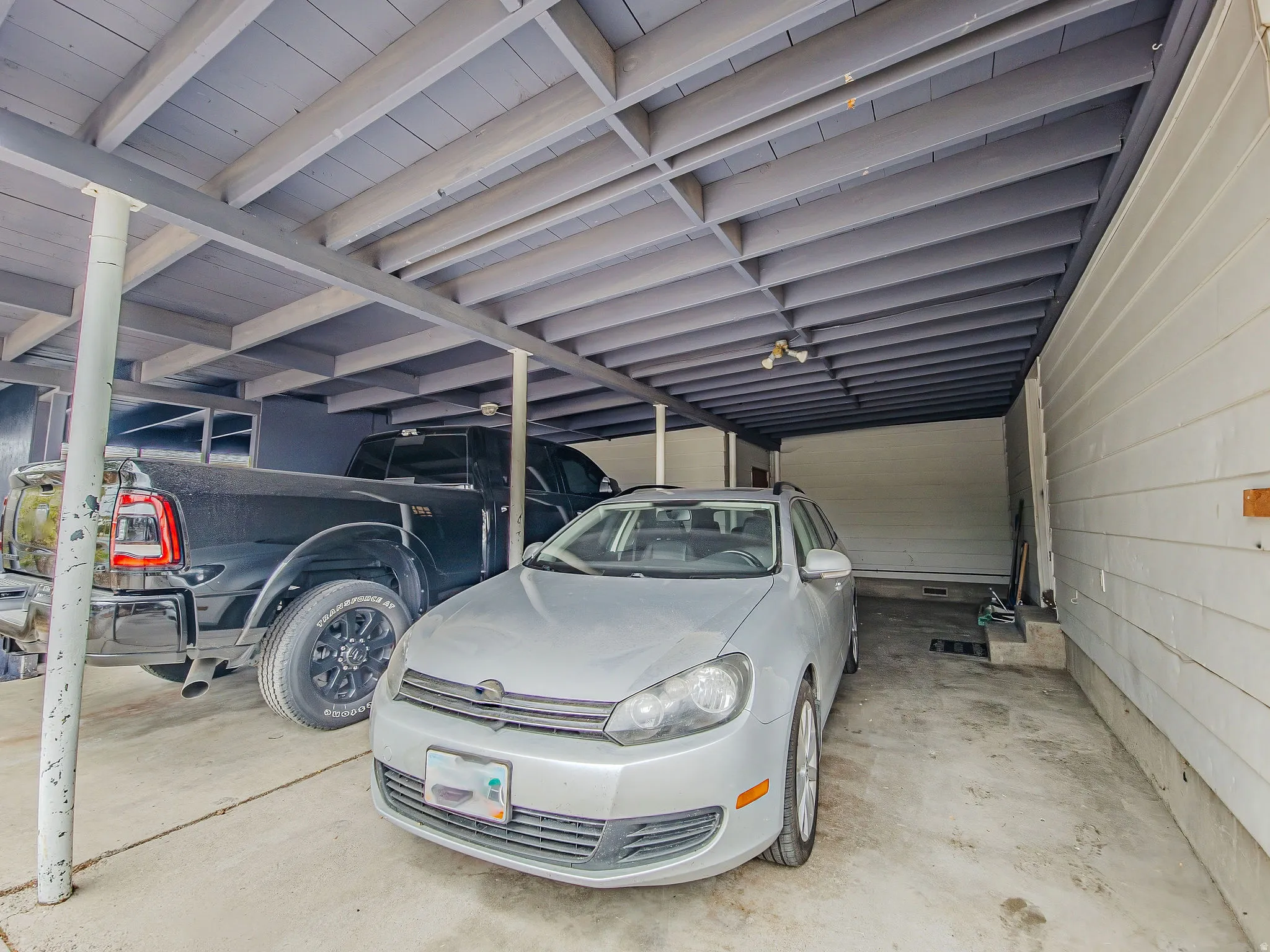 Covered parking area with concrete flooring, wood beam ceiling, and track lighting