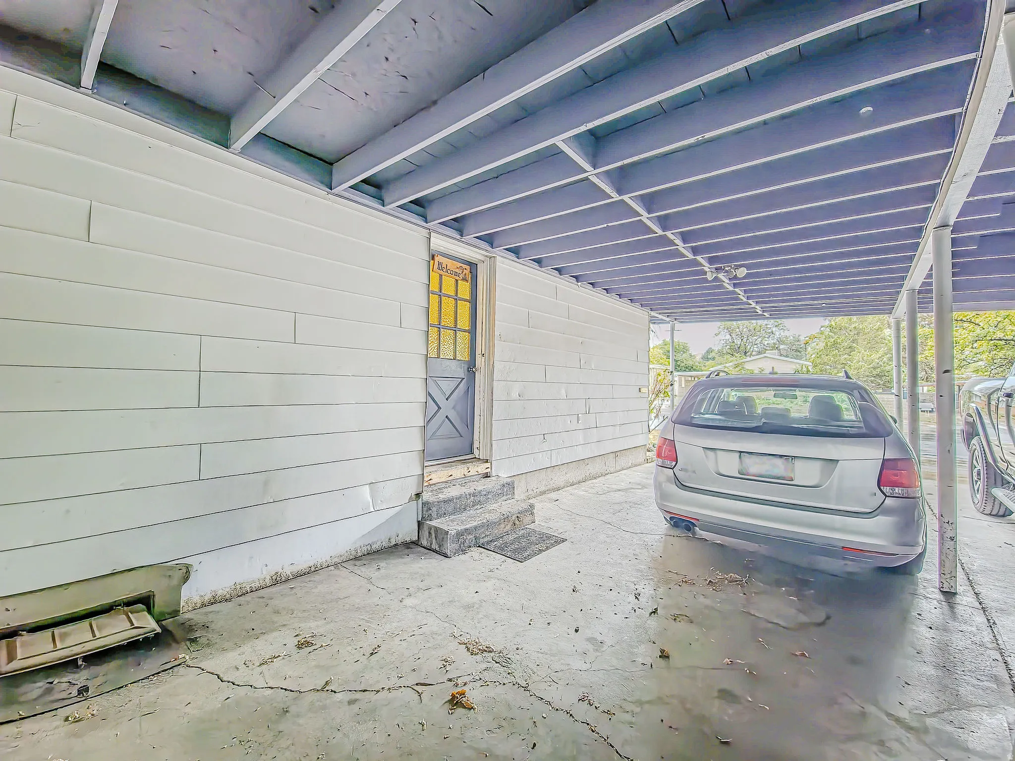 Carport structure with a concrete floor, supporting beams, and a white siding exterior wall