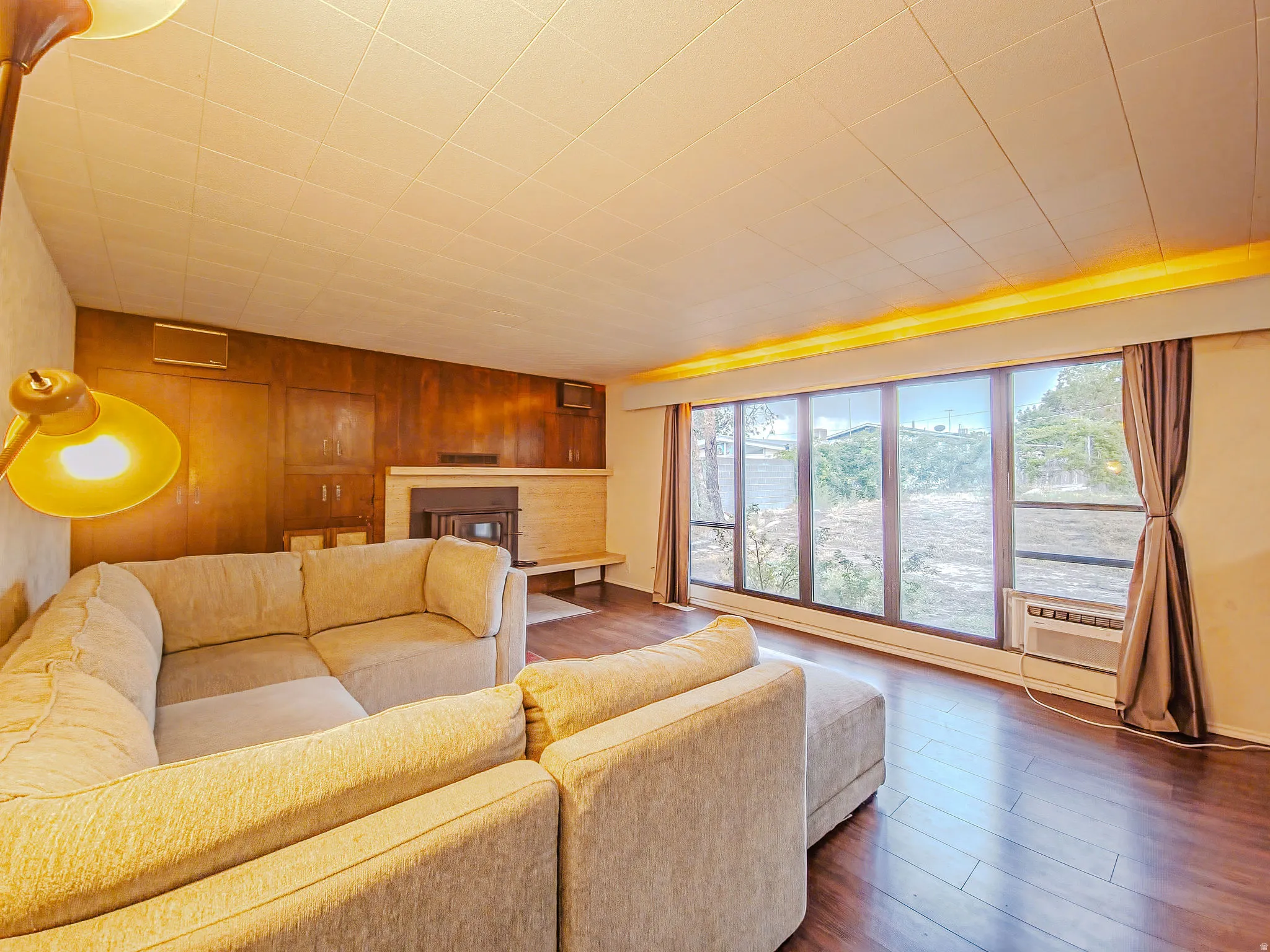 Expansive window wall, rich wood-finish flooring, built-in fireplace, and wood-paneled wall