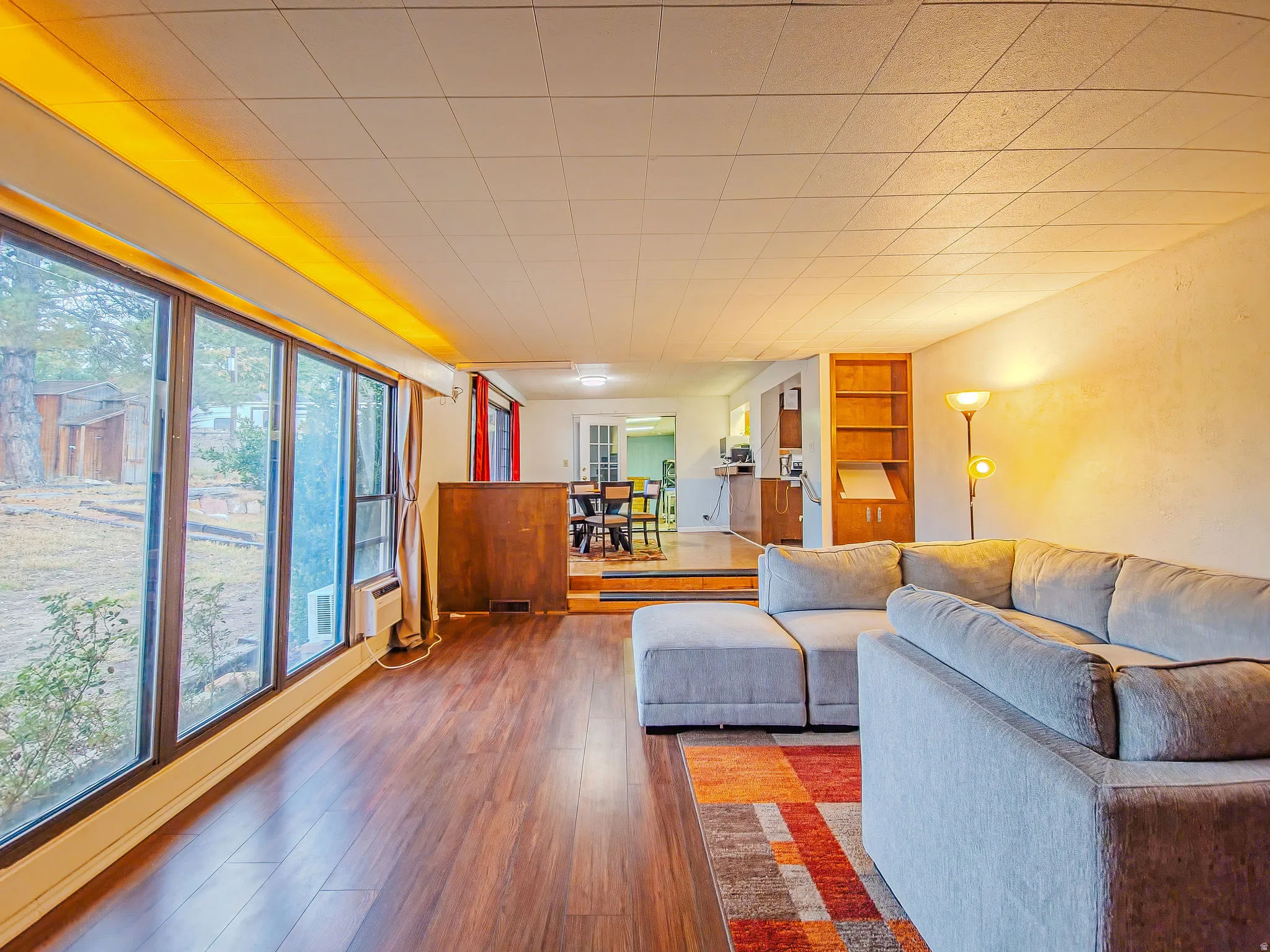 Wood-finish flooring, full-height window wall, built-in shelving, wood-paneled partial wall