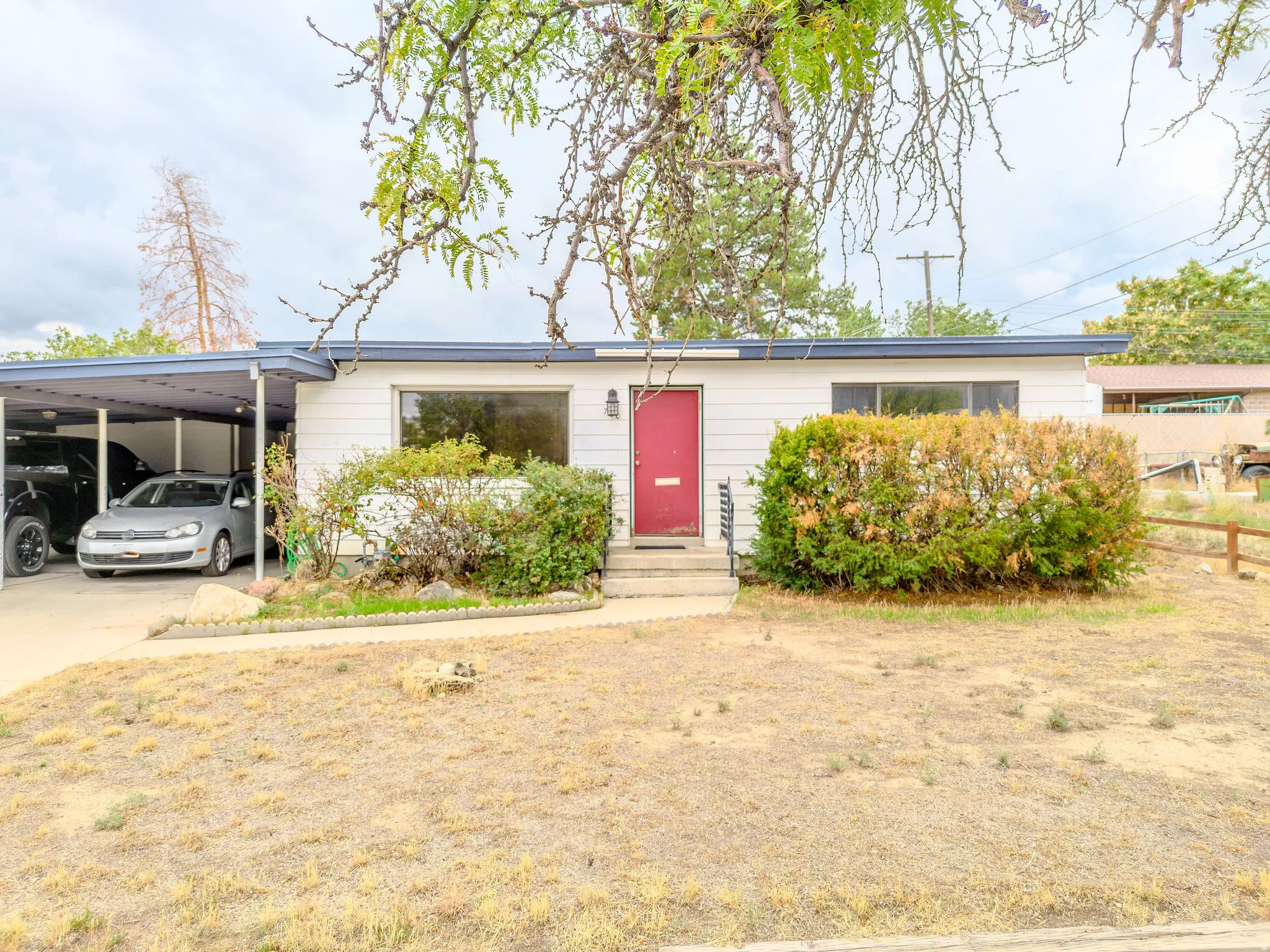 Single-story residence featuring a carport, a vibrant red entry door, and established landscaping