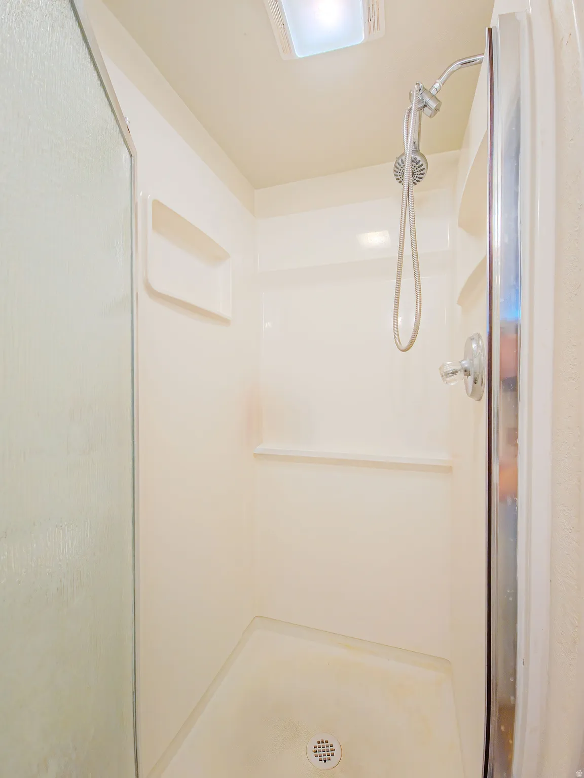 Enclosed shower with a handheld showerhead, built-in shelving, and integrated lighting
