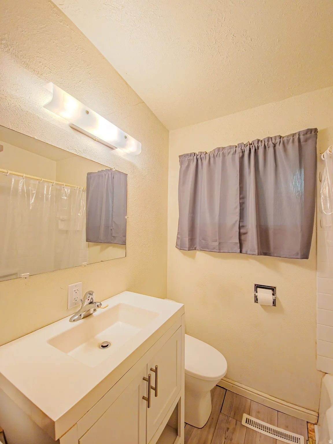 White vanity with integrated sink, chrome faucet, wall-mounted mirror, and wood-finish flooring