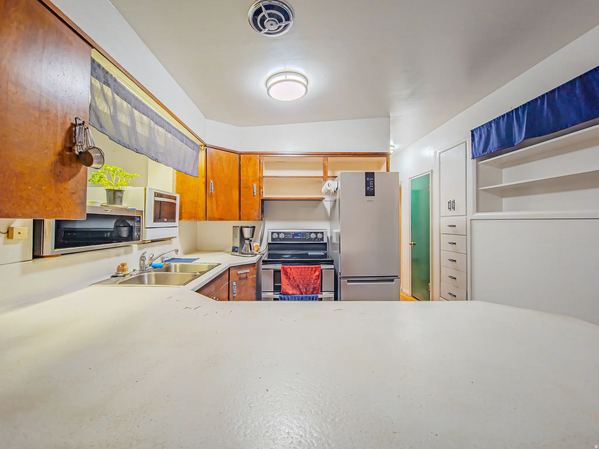 Kitchen featuring wood cabinetry, a double basin stainless steel sink, built-in shelving, and a smooth-top electric range
