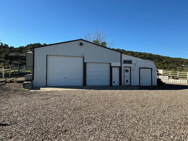 Metal-sided structure featuring two roll-up garage doors, a pedestrian entry door, and an attached shed