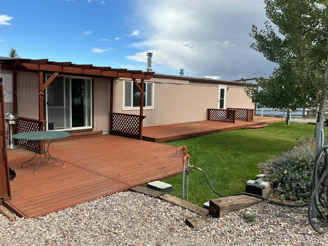Expansive outdoor decking, sliding glass door access, pergola feature, lattice railing accents, and a manicured lawn area