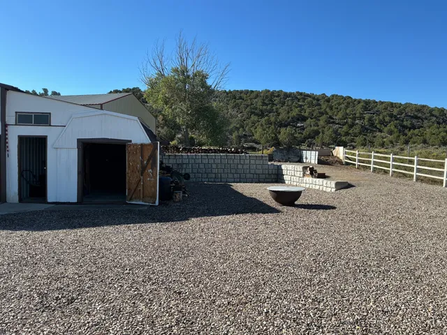 Gravel driveway with a storage structure, white picket fencing, and stone retaining walls