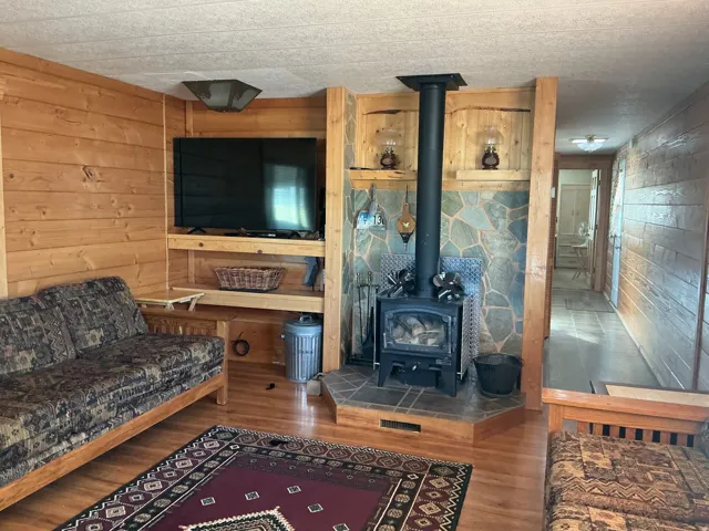 Wood-finish wall paneling, built-in shelving, wood-burning stove with stone surround, and wood-finish flooring