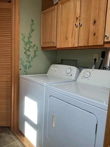 Laundry area with overhead wood-finish cabinetry, tile flooring, and louvered bifold door