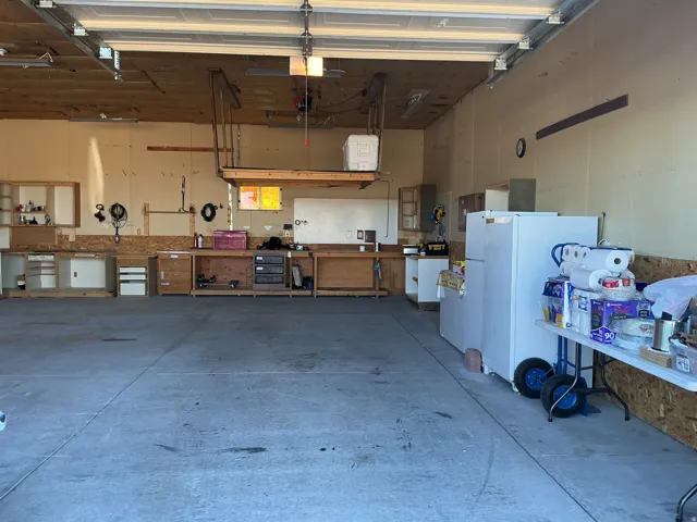 Concrete flooring, built-in workbench with cabinetry, fluorescent overhead lighting, and an elevated storage platform