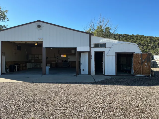 White metal siding structure with a brown trim roofline, dual open garage bays, an open single entry door, and a gravel foreground