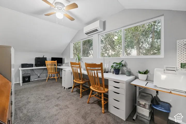 Angled ceiling room with a ceiling fan, two horizontal windows, carpet flooring, and a wall-mounted air conditioning unit