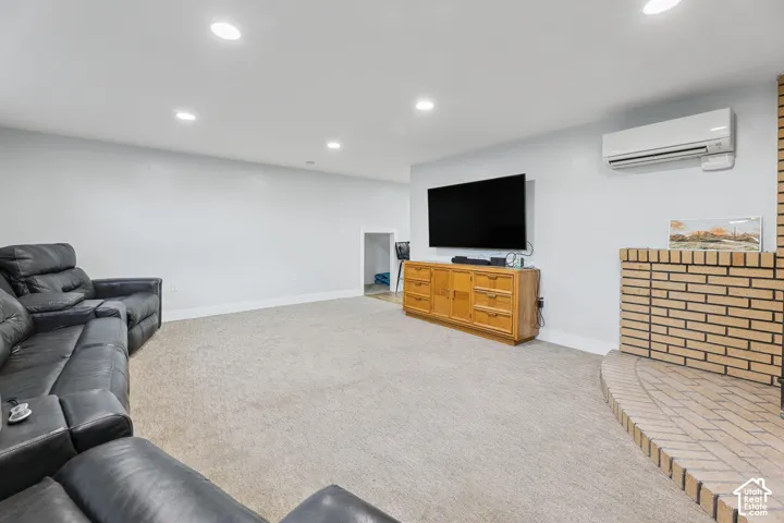 Recessed lighting, light-colored carpeting, brick fireplace, built-in media console, and wall-mounted climate control unit