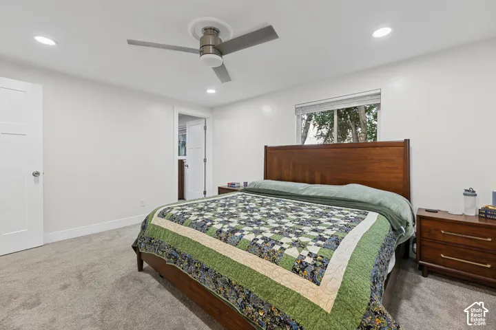 Recessed lighting, ceiling fan, wood-finish headboard, window with privacy blind, gray carpeting