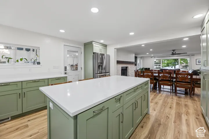 Kitchen featuring a large island with white countertops, green shaker-style cabinetry, wood-finish flooring, and recessed lighting