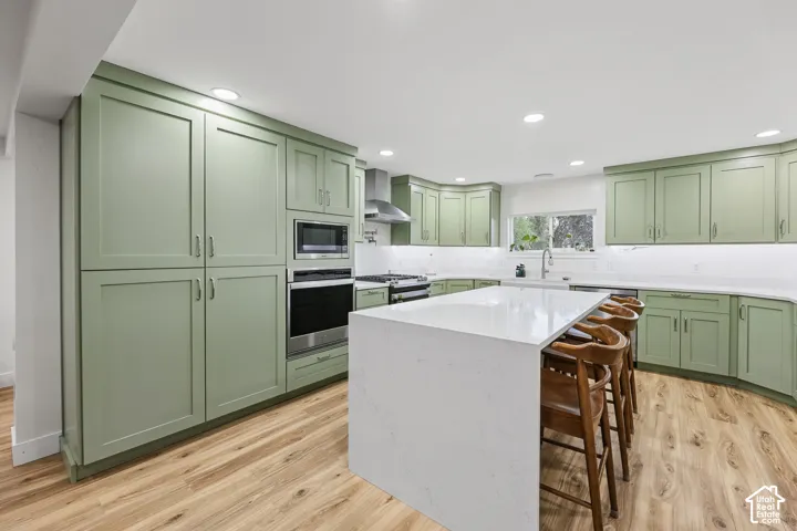 Kitchen featuring extensive sage green cabinetry, a large center island with a light-toned countertop, stainless steel appliances, and wood-finish flooring