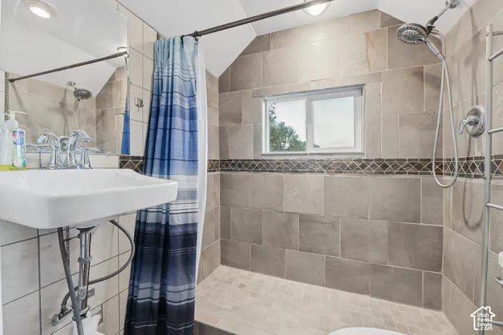 Pedestal sink, tiled shower surround, decorative mosaic tile accent, and a fixed window