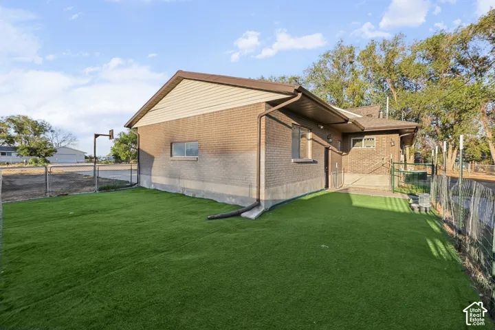 Brick and siding exterior with a brown roof, artificial turf, and chain-link fencing