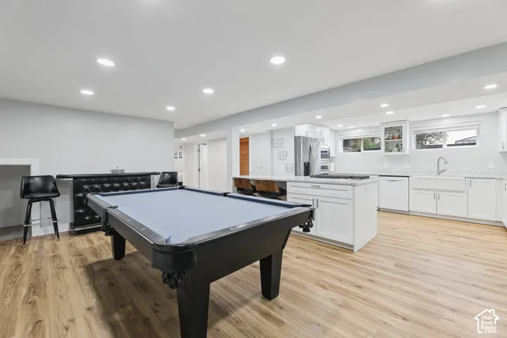 Open-concept living space with wood-finish flooring, recessed lighting, white kitchen cabinetry, a center island, and a farmhouse sink
