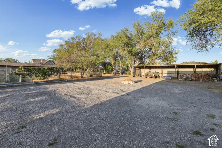 Expansive gravel lot with mature trees, a multi-stall covered structure, and perimeter fencing