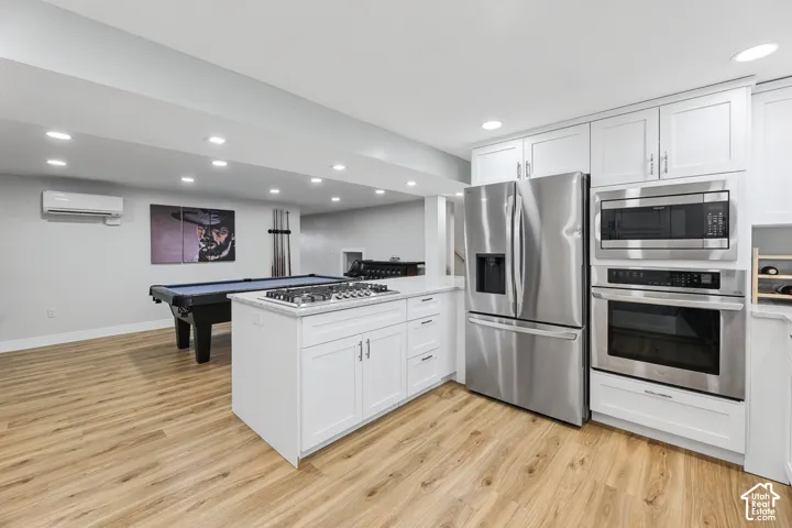 Wood-finish flooring throughout, featuring a kitchen island with cooktop, white cabinetry, stainless steel refrigerator, and integrated stainless steel microwave and oven