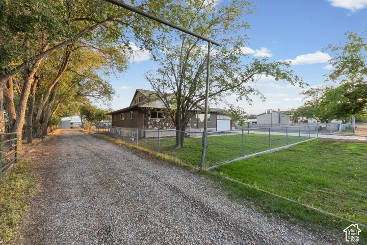 Gravel driveway with mature tree-lined approach, chain-link fencing, and a stone facade on the residence