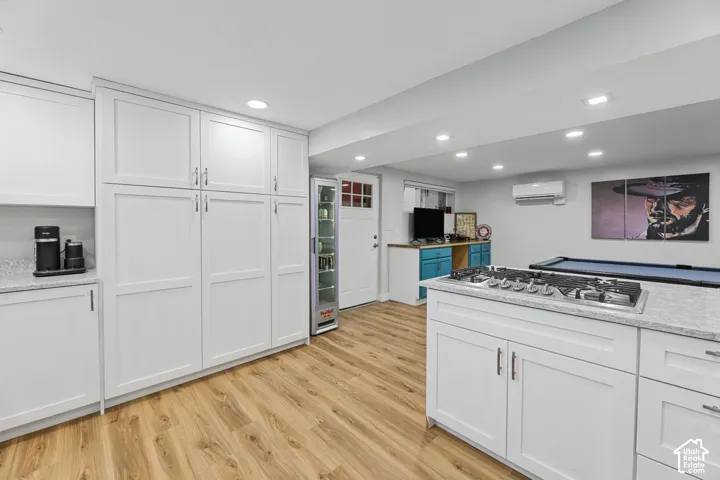 Wood-finish flooring throughout, white shaker-style cabinetry, light-toned granite countertops, recessed lighting, and a built-in gas cooktop