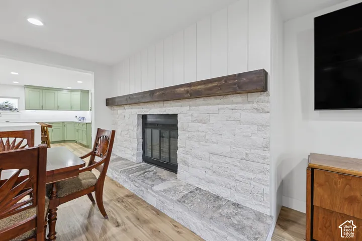 Fireplace with stone surround and hearth, wood mantel, shiplap accent wall, and wood-finish flooring