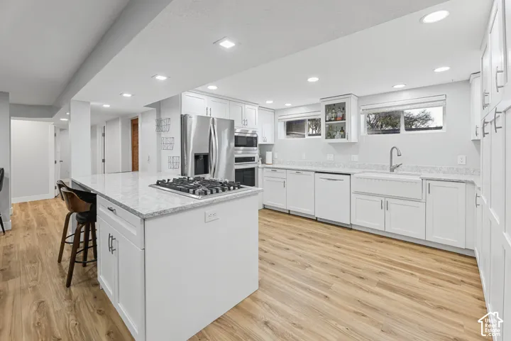Kitchen featuring an island with a gas cooktop, white cabinetry, integrated stainless steel appliances, wood-finish flooring, and recessed lighting