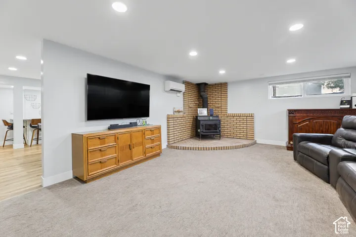 Recessed lighting illuminates the carpeted living area, featuring a brick-surround wood stove and a wall-mounted air conditioning unit