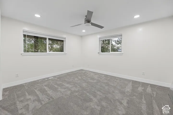 Plush gray carpeting, recessed lighting, ceiling fan, and two windows with blinds