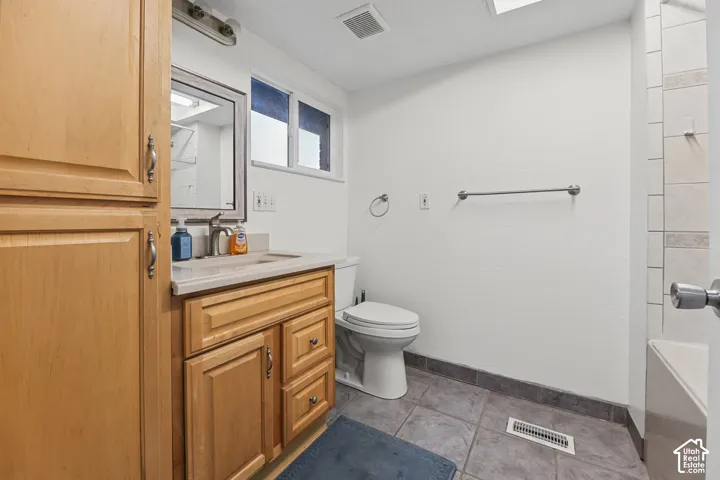 Bathroom featuring a vanity with wood-finish cabinetry, a single basin sink, a framed mirror, and a built-in linen cabinet