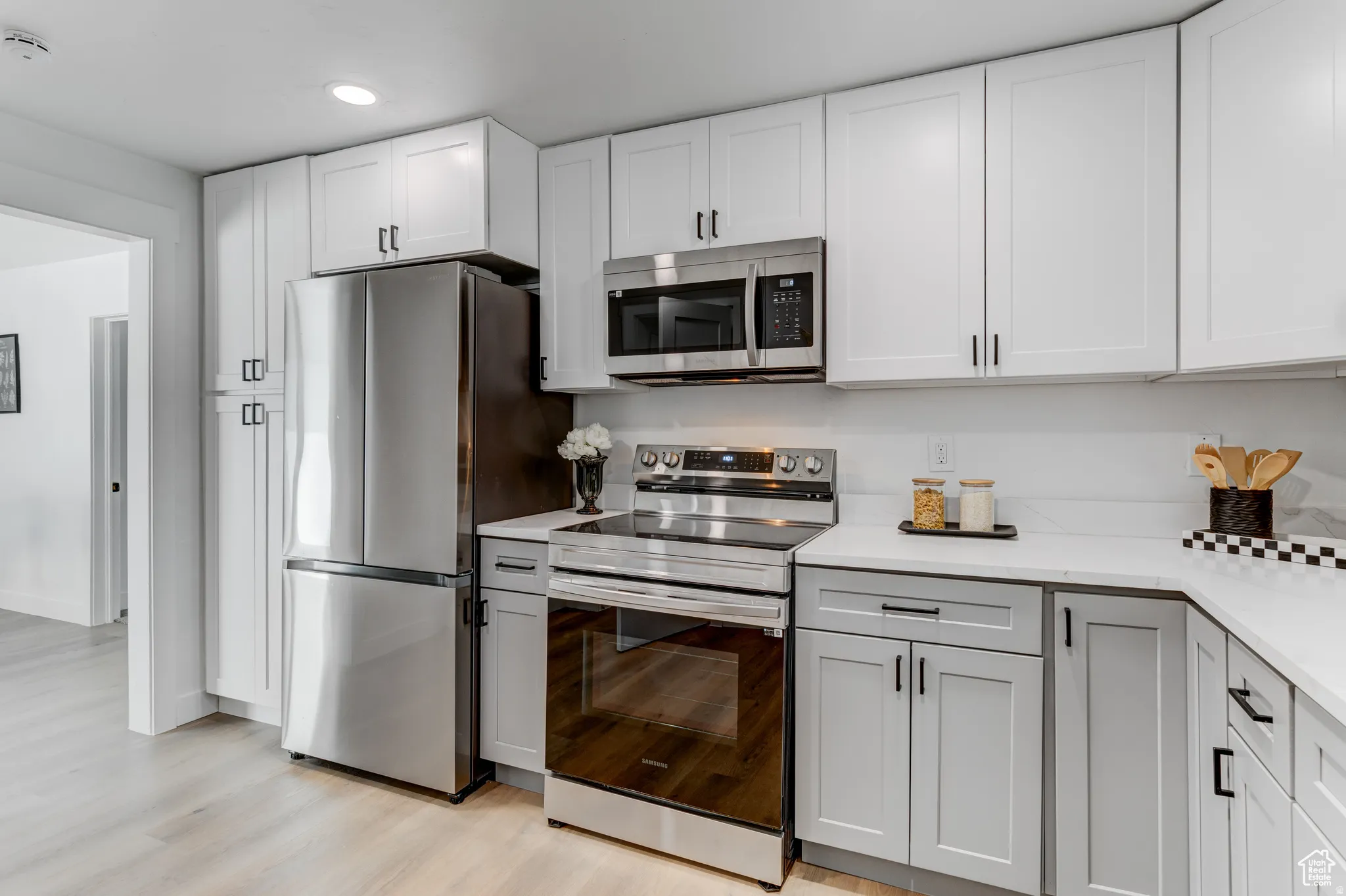 Kitchen featuring stainless steel appliances, white upper cabinetry, gray lower cabinetry, white countertops, and wood-finish flooring