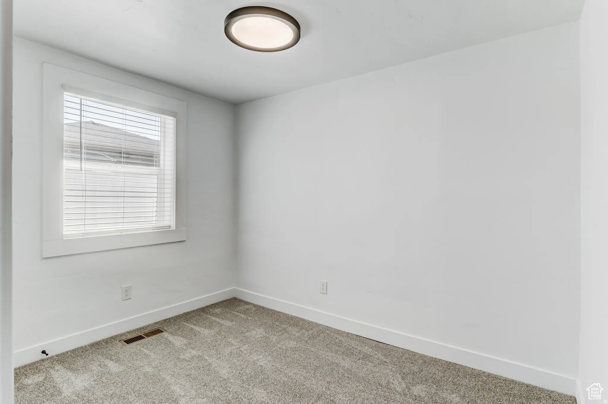 Recessed ceiling light fixture, window with horizontal blinds, light-toned carpeting, and white walls
