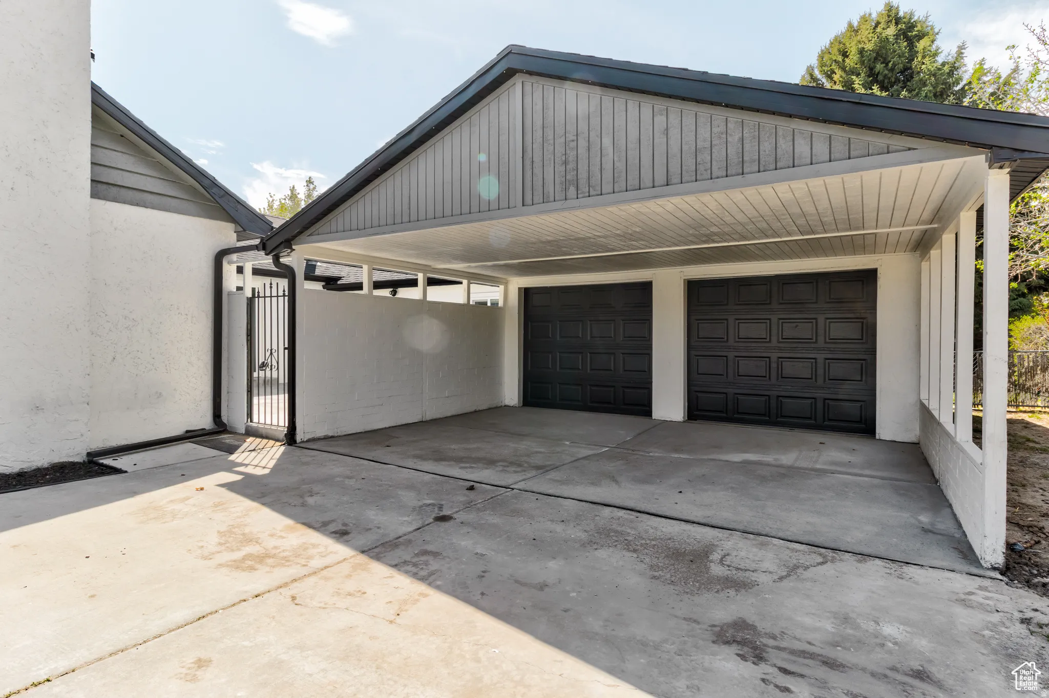 Attached two-car garage with panel doors, covered carport, and concrete driveway