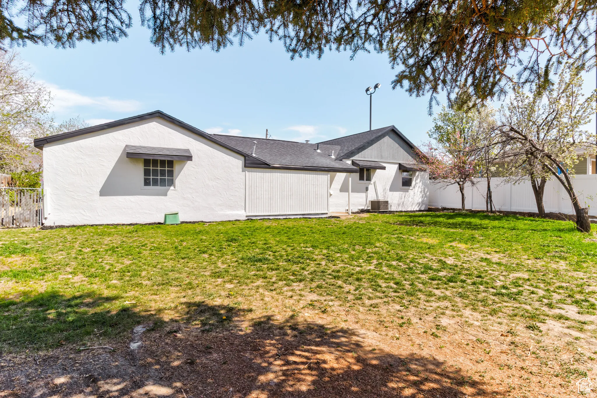 Expansive yard with green lawn, white privacy fencing, and mature trees