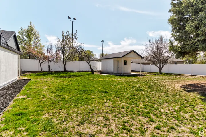 Expansive yard featuring a detached storage shed with covered entry, a full privacy fence, and mature trees