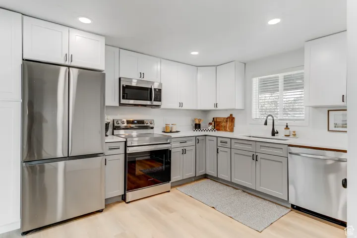 Well-appointed kitchen featuring stainless steel appliances, shaker-style cabinetry, light-toned wood-finish flooring, a white countertop, and a built-in sink with a matte black faucet