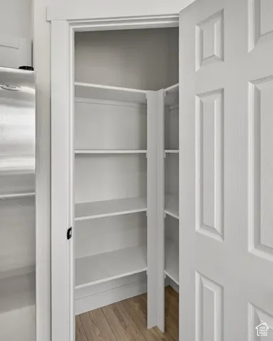 Pantry with multiple white shelves, wood-finish flooring, and a paneled door
