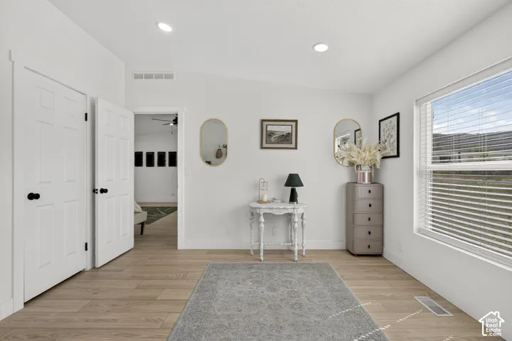 Recessed ceiling lighting, light wood-finish flooring, white paneled doors with matte black hardware, and a large window with horizontal blinds