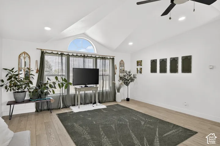 Vaulted ceiling with an arched window, wood-finish flooring, and recessed lighting