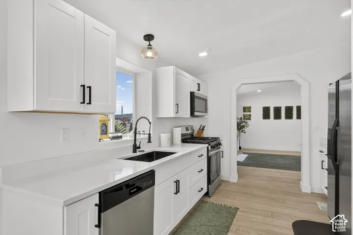 Kitchen featuring white shaker cabinetry, stainless steel appliances, a black sink, a modern black faucet, and wood-finish flooring