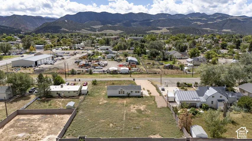 Expansive lot featuring a single-story residence with a light-colored exterior and a dark roof, surrounded by a mountain range backdrop